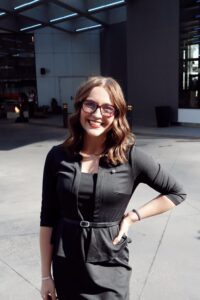 Brunette woman with glasses posing with hand on hip.