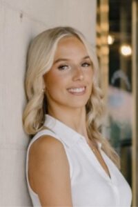 Blond woman in white blouse leaning against wall