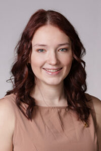Brunette woman in tan sleeveless top.