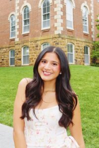 Brunette woman standing in front of green lawn and brick college campus building