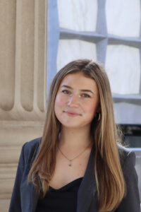 Woman in black blazer in front of column.