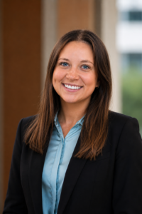 Brunette woman in blue button up shirt and black blazer.