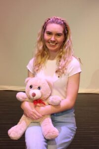 Woman with blonde curly hair holding teddy bear on lap.