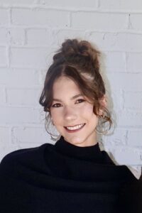 Woman with dramatic up-do in black sweater smiling.
